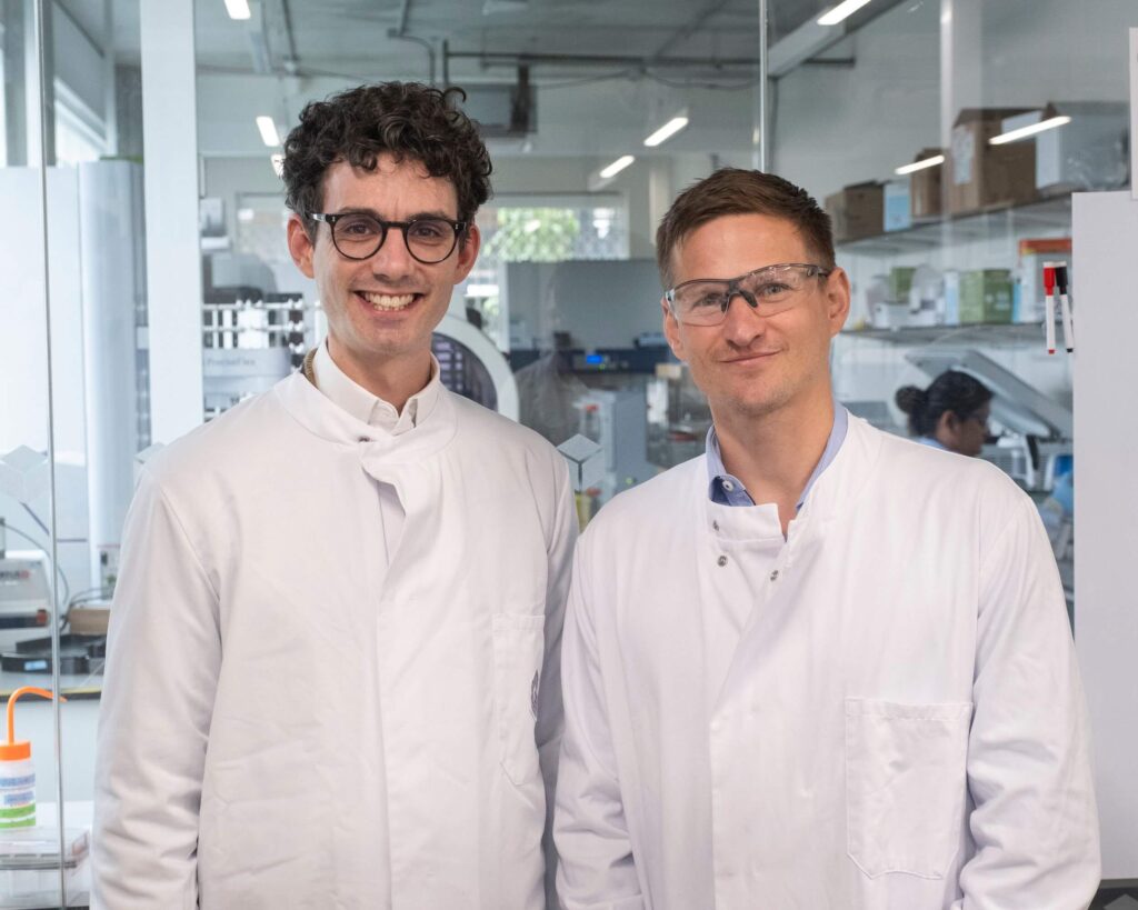 James Field (LabGenius) and Oliver Hardick (M Ventures) standing in a lab wearing white lab coats and safety glasses